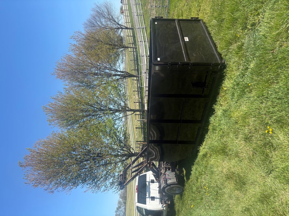 Black roll-off dumpster being delivered in a green pasture